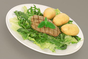 A plate of green leaf salad with baby potatoes and steak