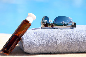 Sunglasses, towel and oil bottle by the swimming pool