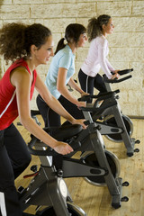 Fototapeta na wymiar Three happy, young women working out on exercise bicycle 