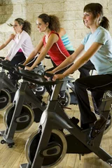 Foto op Plexiglas The group of women training on exercise bikes at the gym.  © Tomasz Trojanowski