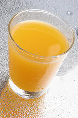 Orange juice on glass with drops on reflecting background