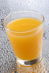 Orange juice on glass with drops on reflecting background