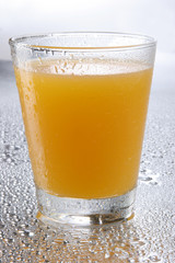 Orange juice on glass with drops on reflecting background