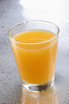 Orange juice on glass with drops on reflecting background