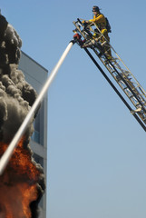 Fototapeta premium A Fire Man on a lift up high hosing a fire below him