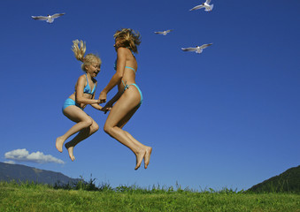 mother and daughter jumping in a meadow