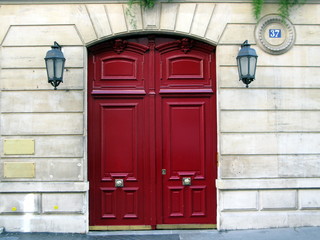 Porte rouge sur façade de pierre avec lanternes à Paris.
