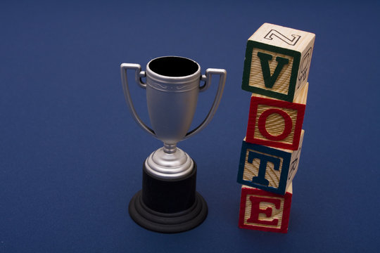 Trophy with vote alphabet blocks on a blue background