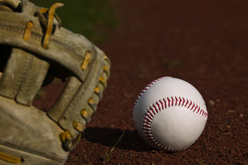 Baseball and a glove sitting on the dirt of a diamond