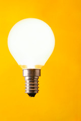 Shining light bulb close-up over yellow background