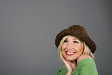 A blonde model in a brown hat smiling and looking up