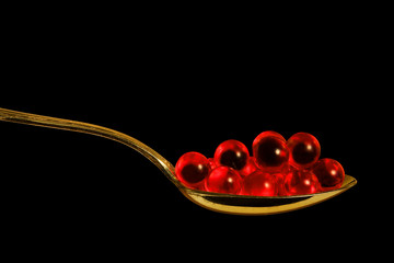 Red pills in a teaspoon, close-up, isolated on black