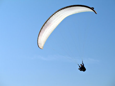 A paraglider il flying in the blue sky with his white paraglide