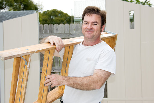 Friendly handyman carrying a ladder and smiling.