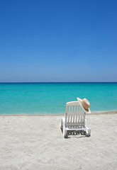 Empty tropical beach chair with hat  at shoreline 