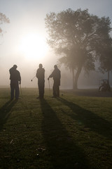 Early morning golfers silhouetted in a dense fog