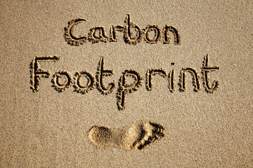 Carbon footprint written in sand on a beach.