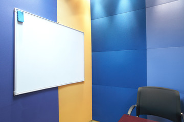 Whiteboard and a grey office chair against blue and yellow 