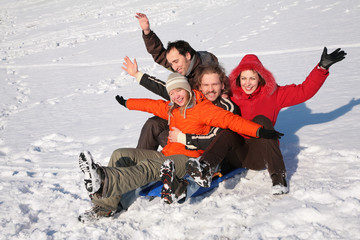 group of friends sit on plastic sled on snow