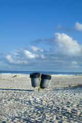Two garbage cans on beach with blue sky