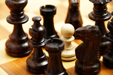 white pawn chessman surrounded by black pieces