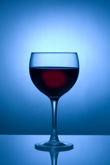 Glass of red wine silhouetted against a blue spotlight 