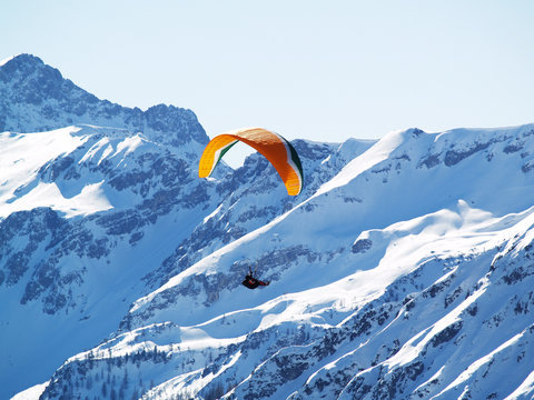 A flying paraglider in mountains in the winter.