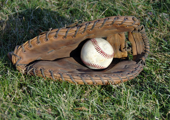 Baseball glove and ball laying in the grass.