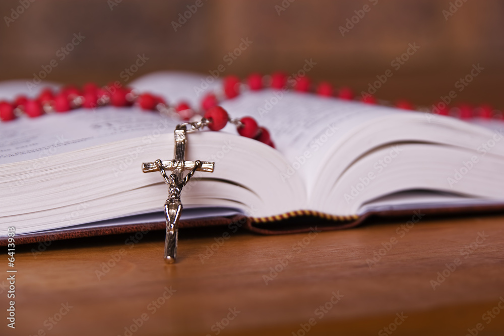 Wall mural a bible open on a table with a red rosary place ontop of it.