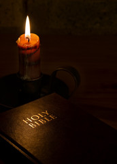 A moody image of The Holy Bible next to a candle. 