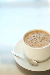Fresh foamy cafe latte in white coffee cup on a silver 