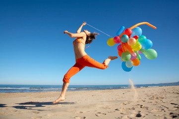 Fototapeta na wymiar happy girl jumping on the beach with colorful balloons