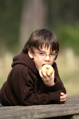 garçon avec des lunettes entrain de manger une pomme