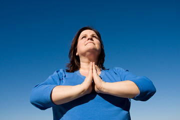 Woman praying outdoors against a vivid blue sky.