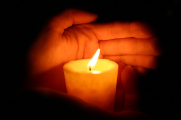 hands keeps burninging candle in the dark