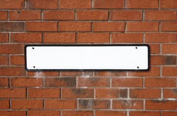 Blank white British street sign on a red brick wall.