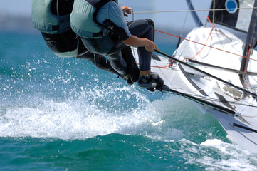 Sailors splash through the waves during a regatta. - obrazy, fototapety, plakaty