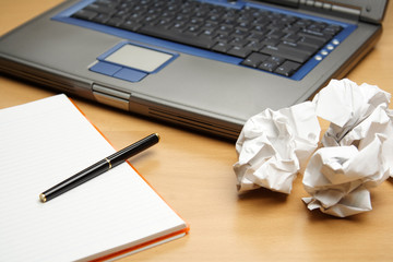 A laptop and a notebook with crumpled paper