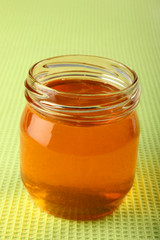 Honey in glass pot on green background