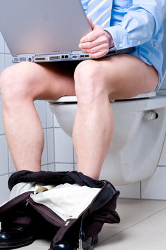 Mann mit blauem Hemd auf Toilette mit Laptop