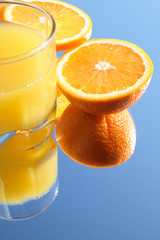 Glass of orange juice and incised orange on blue background