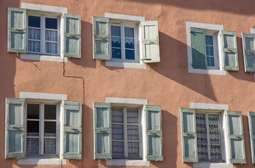 Fototapeta na wymiar Façade aux murs roses avec six fenêtres aux volets ouverts
