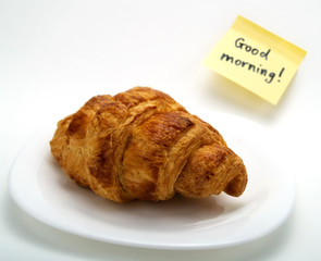 A croissant in a white plate and a yellow note
