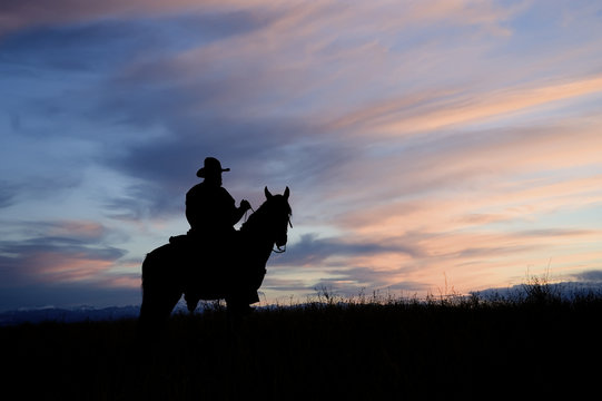 Cowboy on horseback back lit by the dawn sky