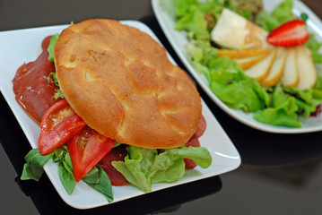 Sandwich of tomato, salad and ham with salad in the background 