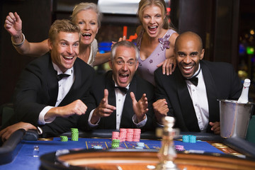 Five people in casino playing roulette smiling