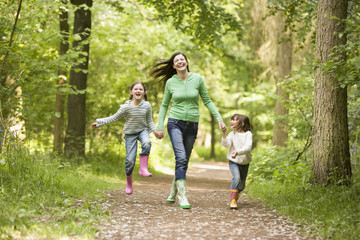 Fototapeta premium Mother running along woodland path with 2 childrren
