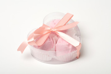 Fototapeta na wymiar Little pink cakes in a heart shaped box over white