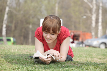 girl lays on a grass and reads the book