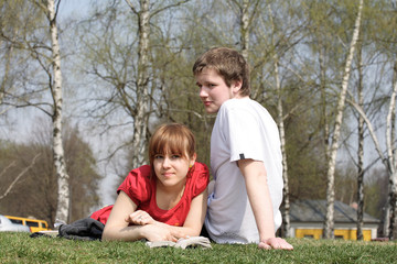 Friends. The young man and the girl sit on a grass in park.